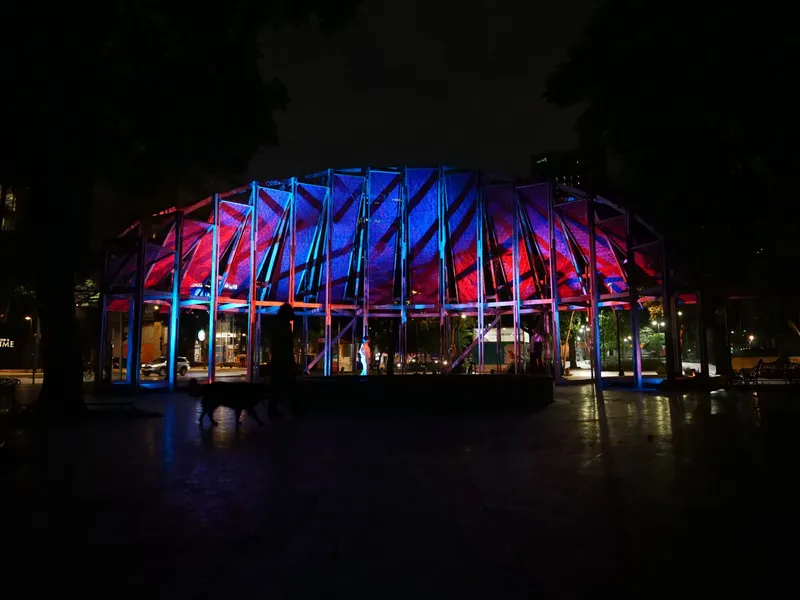 Night view of the illuminated pavilion with blue and red lighting on timber frame and fabric roof