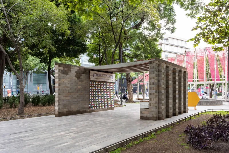 Outdoor pavilion with perforated brick walls and a timber roof in a tree-lined public plaza