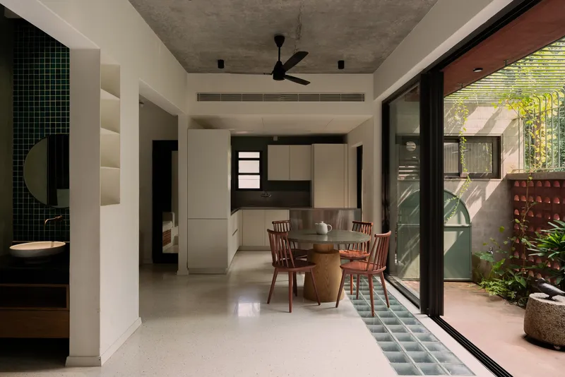 Open-plan dining area with terrazzo flooring opening onto a planted courtyard through sliding glass doors
