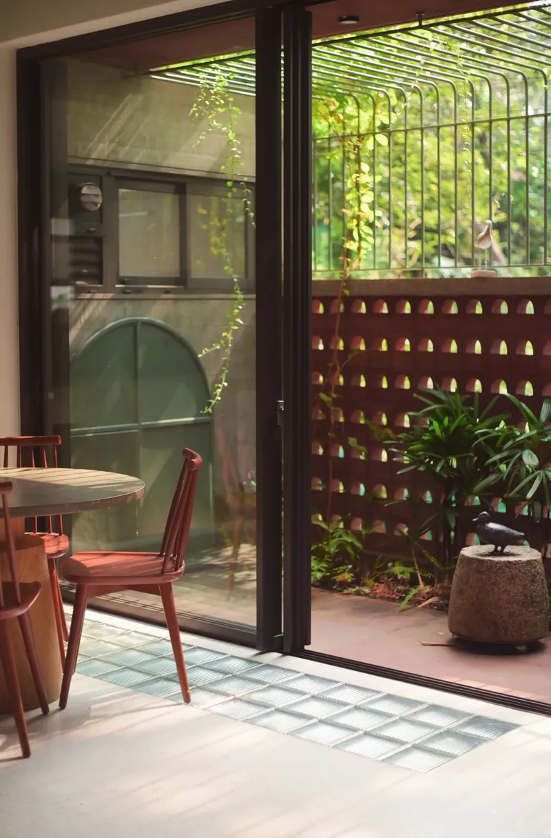 View from interior through glass doors to courtyard with perforated terracotta screen wall and curved metal trellis