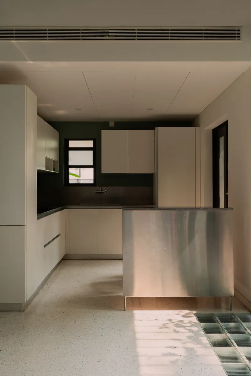 Kitchen with cream cabinetry and steel breakfast counter above terrazzo floor with green tile inset