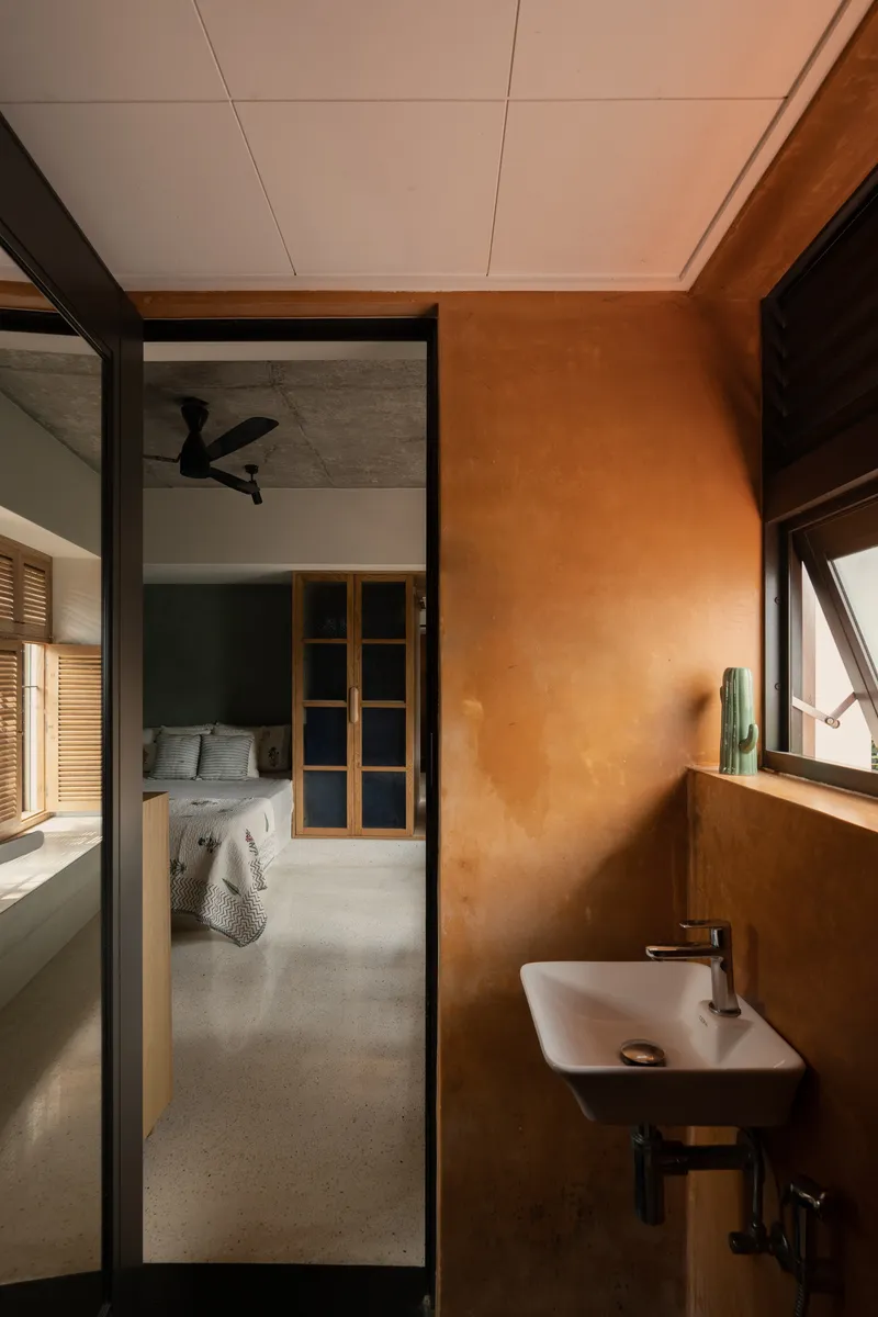Bathroom with terracotta plaster walls and view through glazed door to bedroom with ceiling fan