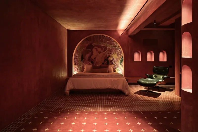 Bedroom enveloped in terracotta plaster with arched headboard niche and tiled floor with brass inlay