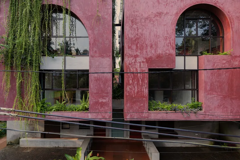 Street-level view of the pink facade showing arched openings and planted terrace beds with cascading greenery