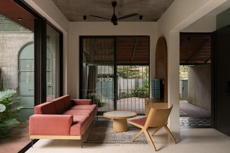 Living room with exposed concrete ceiling and full-height glazing overlooking a planted courtyard with bamboo screens