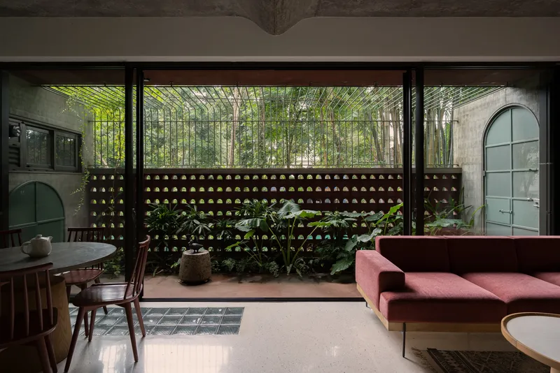 Living space opening onto courtyard through perforated brick screen wall with bamboo and tropical plants beyond