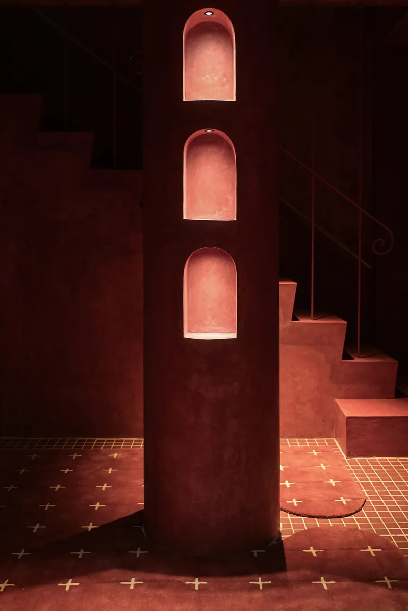 Vertical stack of three arched niches illuminated in red plaster wall beside curving stair