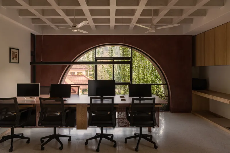 Workspace with coffered ceiling and arched window framed by a maroon wall overlooking greenery