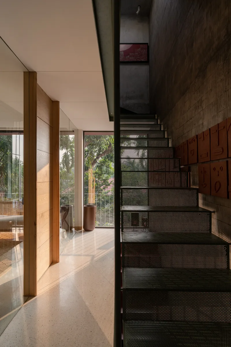 Perforated metal staircase rising beside timber storage wall and glazed doors with garden beyond