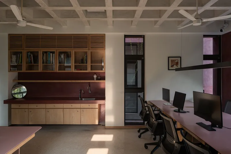 Office workspace with timber cabinetry and maroon backsplash beneath a coffered ceiling with natural light