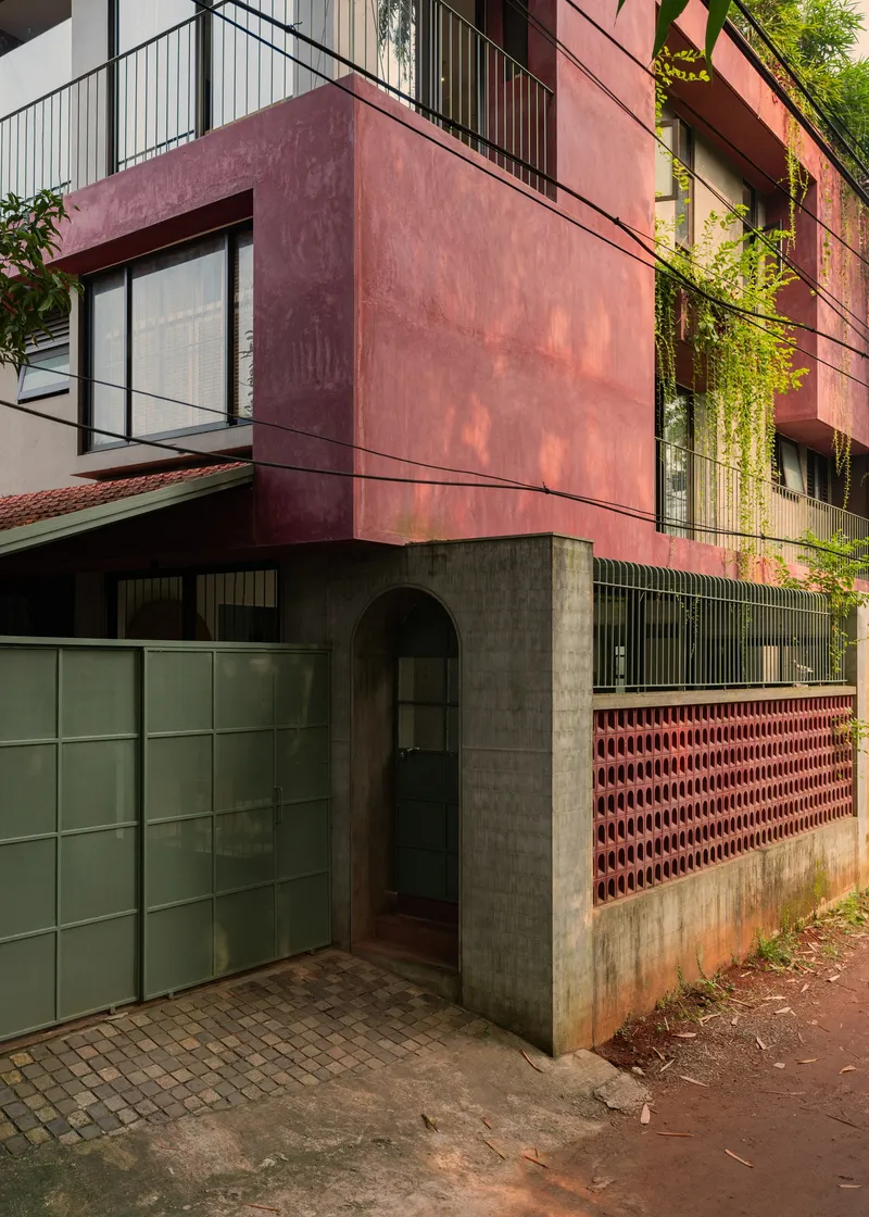 Corner entry with concrete portal and terracotta perforated screen wall beneath cantilevered red oxide volume