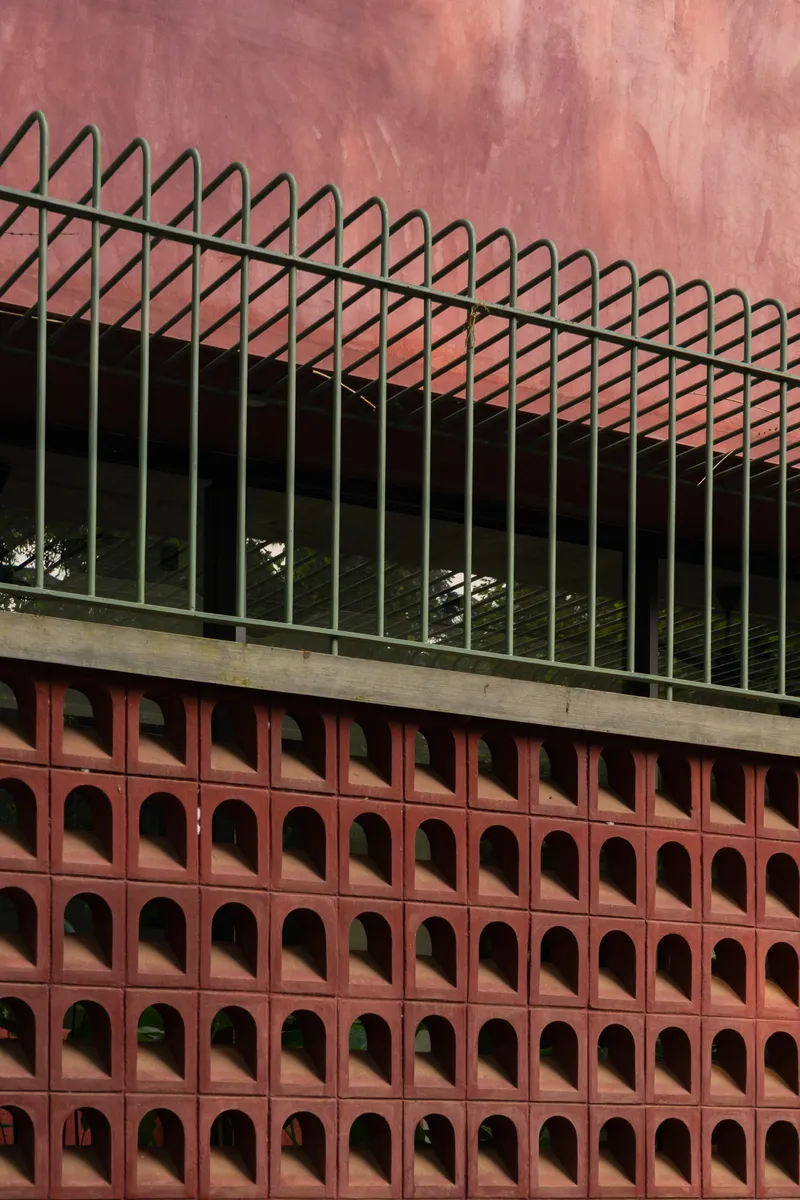 Close-up of the terracotta perforated screen with triangular metal railing above the concrete ledge