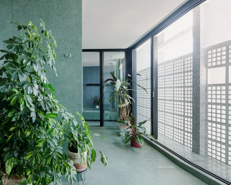 Corridor with green terrazzo flooring and white glass block screen filtering daylight past potted plants