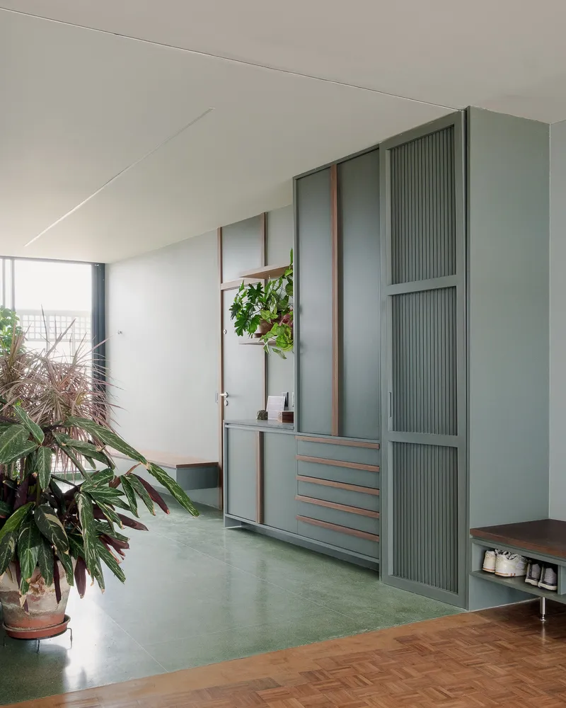 Built-in storage unit with fluted green panels and timber frames beside parquet flooring and potted plants