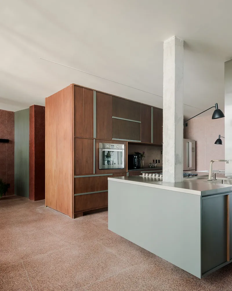 Open kitchen with timber cabinetry and pale green island under a concrete column and pendant lights