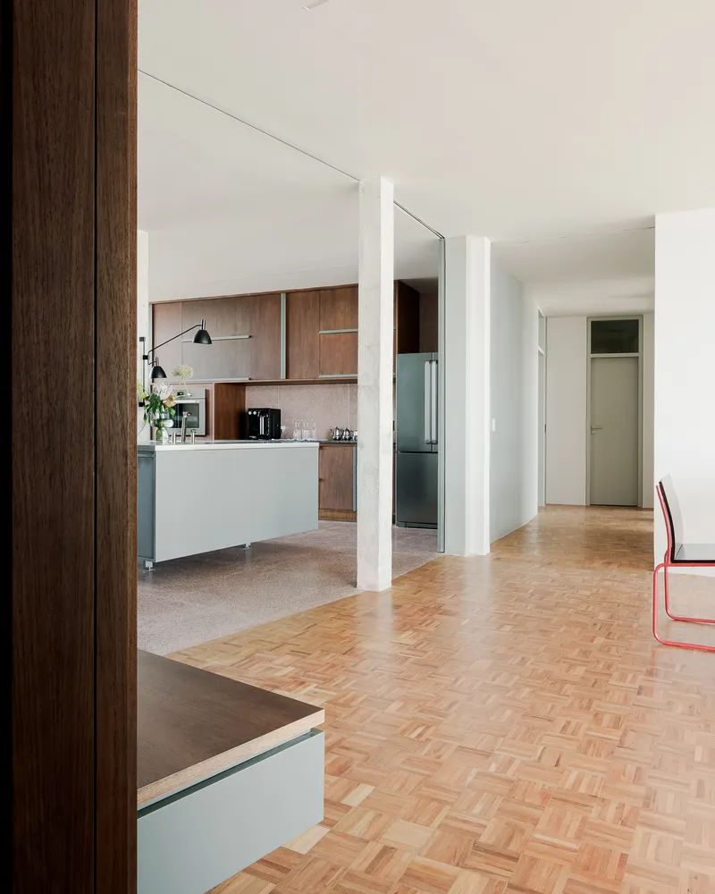 Open living space with herringbone parquet flooring transitioning to terrazzo in the kitchen area