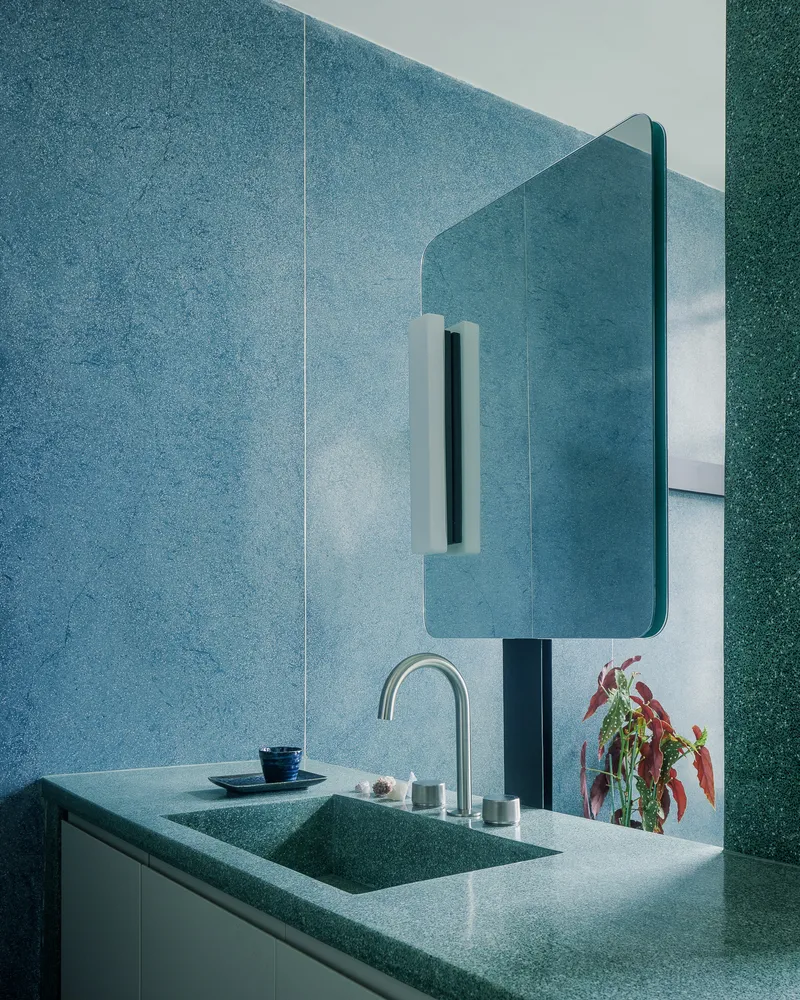 Bathroom vanity with integrated terrazzo sink and rounded mirror against blue mosaic tile walls