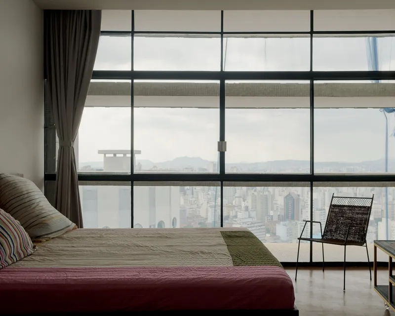 Floor-to-ceiling glazing framing a hazy cityscape with dark curtains and woven lounge chair