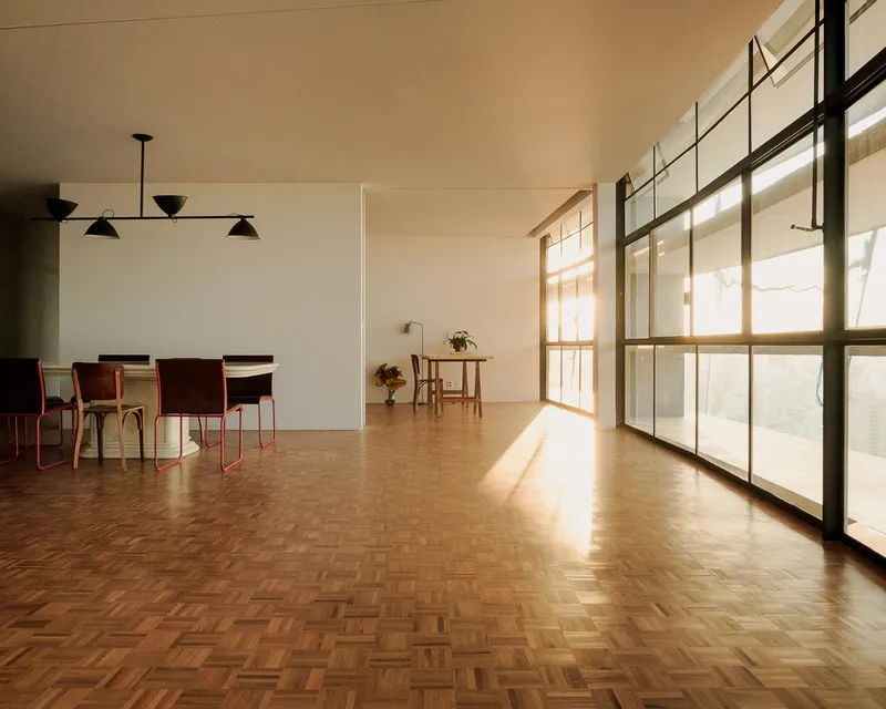 Dining area with steel-framed glazing along one wall casting afternoon sunlight across the parquet floor