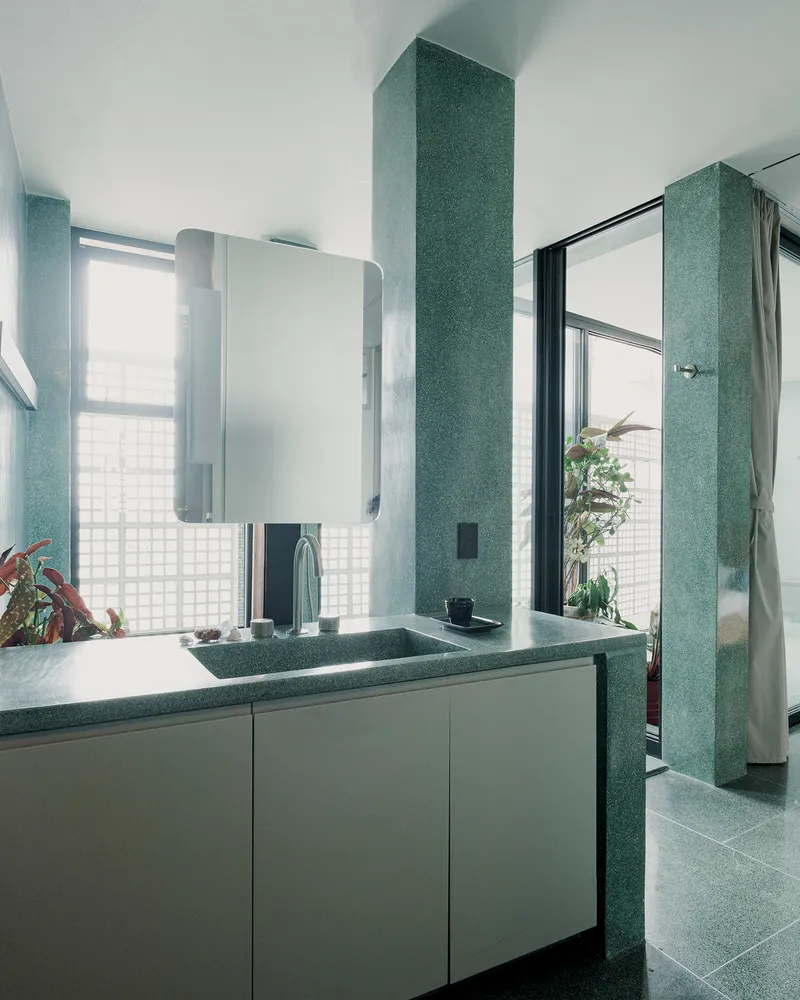 Bathroom with green terrazzo walls, floating vanity, and glass block window in diffused daylight