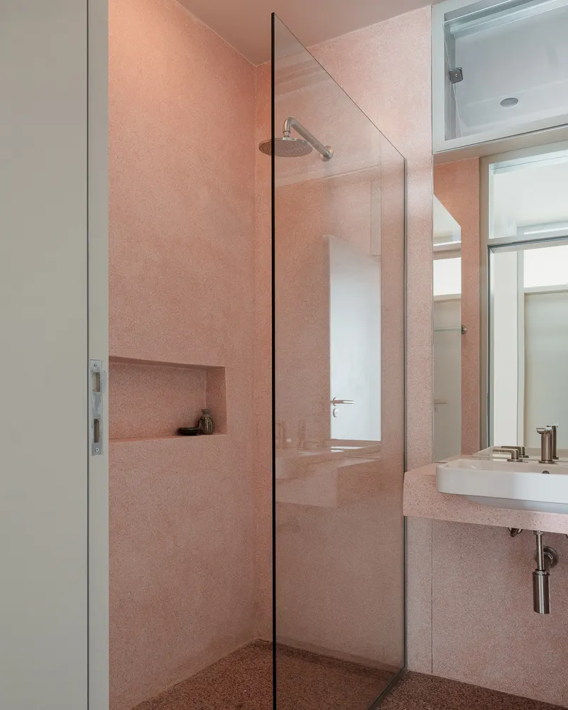 Pink terrazzo bathroom with glass shower partition and recessed wall niche under soft ceiling light