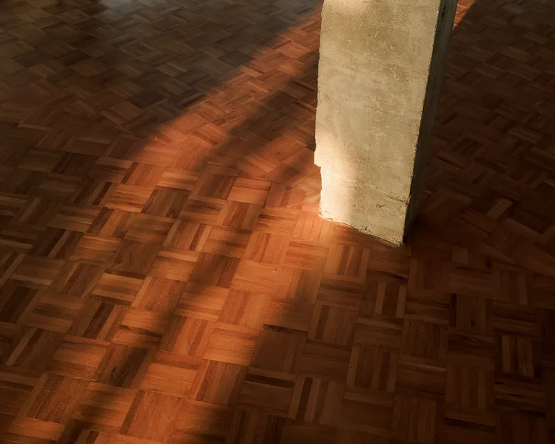 Herringbone parquet floor meeting a textured concrete column base in warm afternoon sunlight