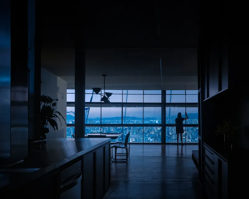 Interior view through a kitchen island toward floor-to-ceiling glazing overlooking a cityscape at dusk