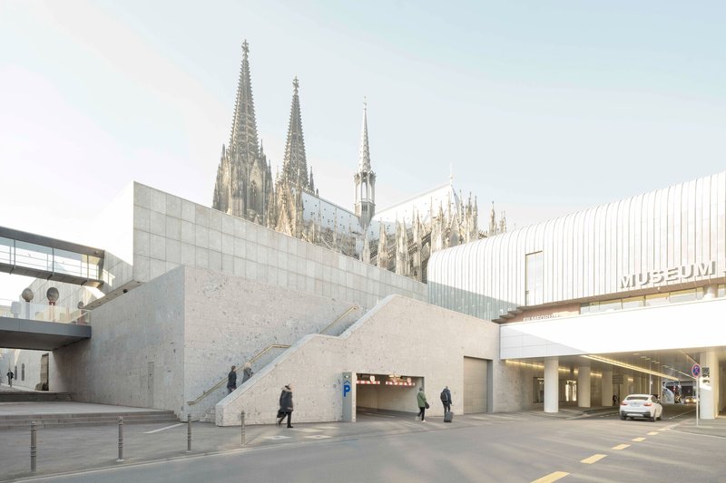 Angled concrete volumes creating a sunken entry with exterior stairs and scattered pedestrians