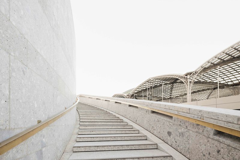 Concrete staircase curving upward alongside a cast wall under a lattice roof canopy