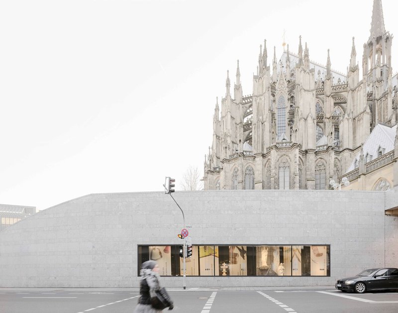 Concrete facade with horizontal storefront windows and a blurred pedestrian crossing the street