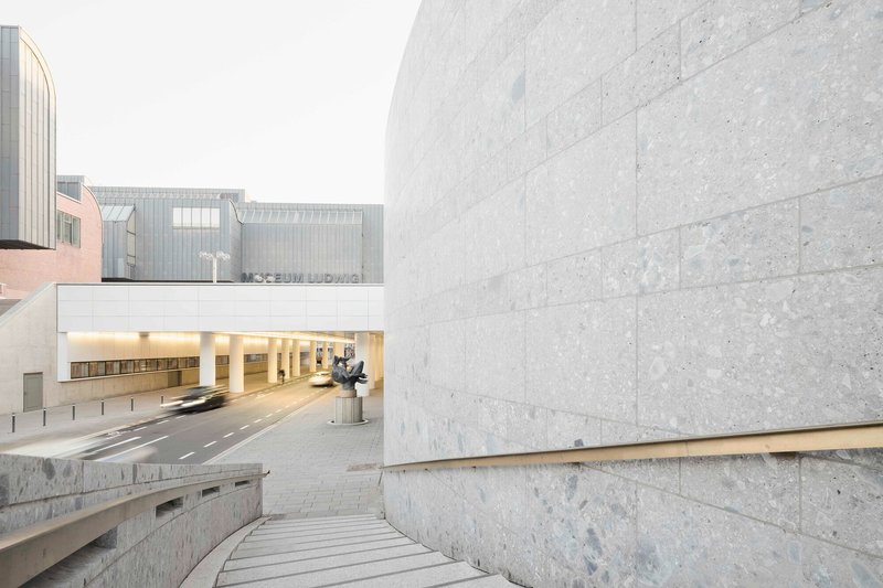 Stone steps descending between limestone walls toward an illuminated tunnel opening with sculpture visible beyond