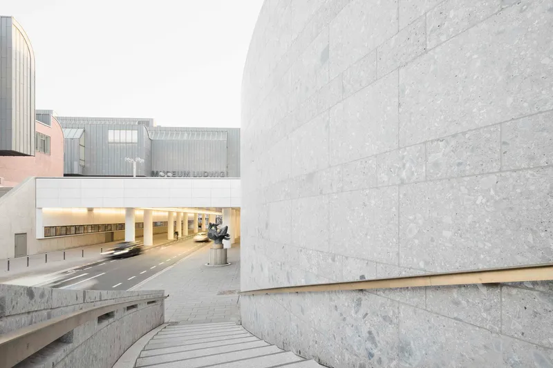 Stone steps descending between limestone walls toward an illuminated tunnel opening with sculpture visible beyond