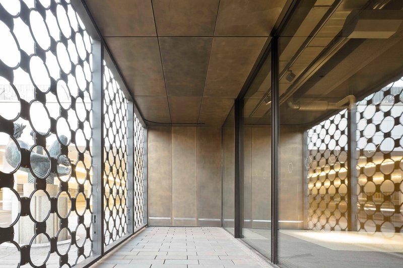 Interior corridor with perforated circular metal screens flanking both sides and polished stone flooring