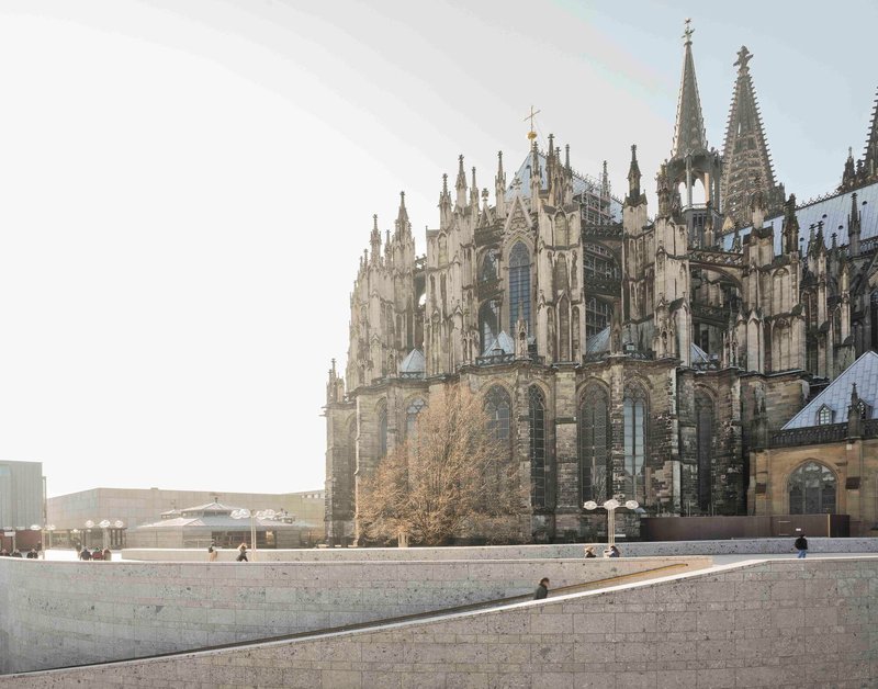 Wide stone plaza with scattered visitors beside the cathedral apse and bare tree in daylight