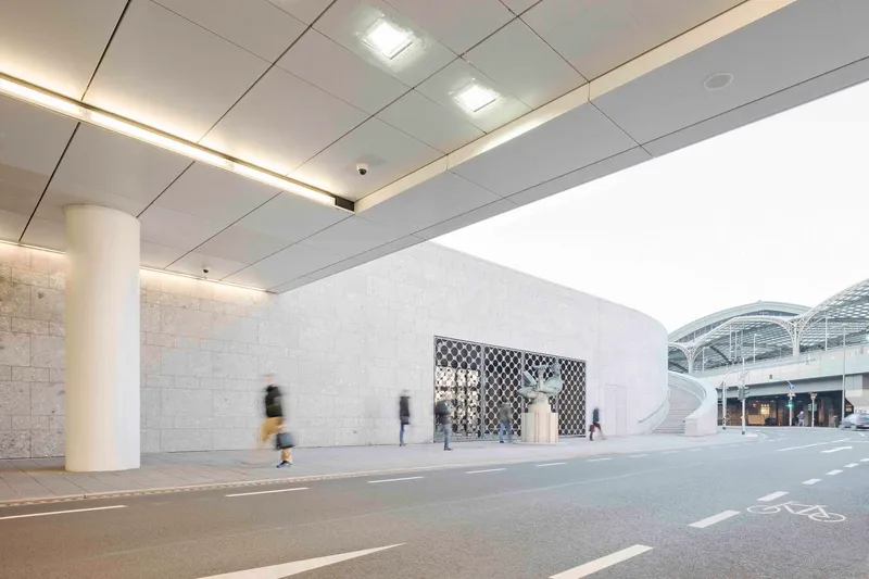 Interior passage with dropped ceiling panels and cylindrical columns alongside a curved stone wall