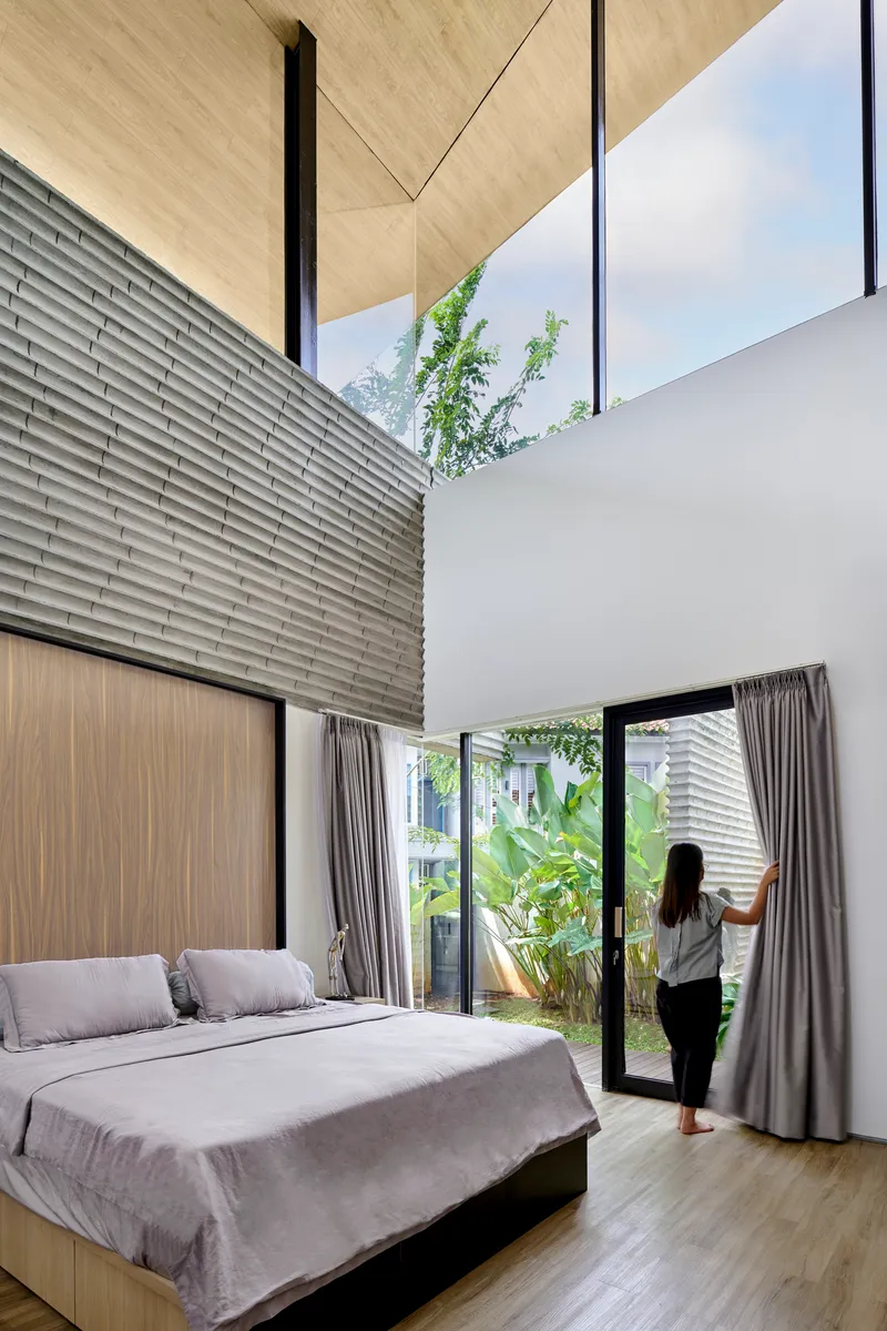Bedroom with sliding glass doors to garden, plywood ceiling and person opening curtain in morning light