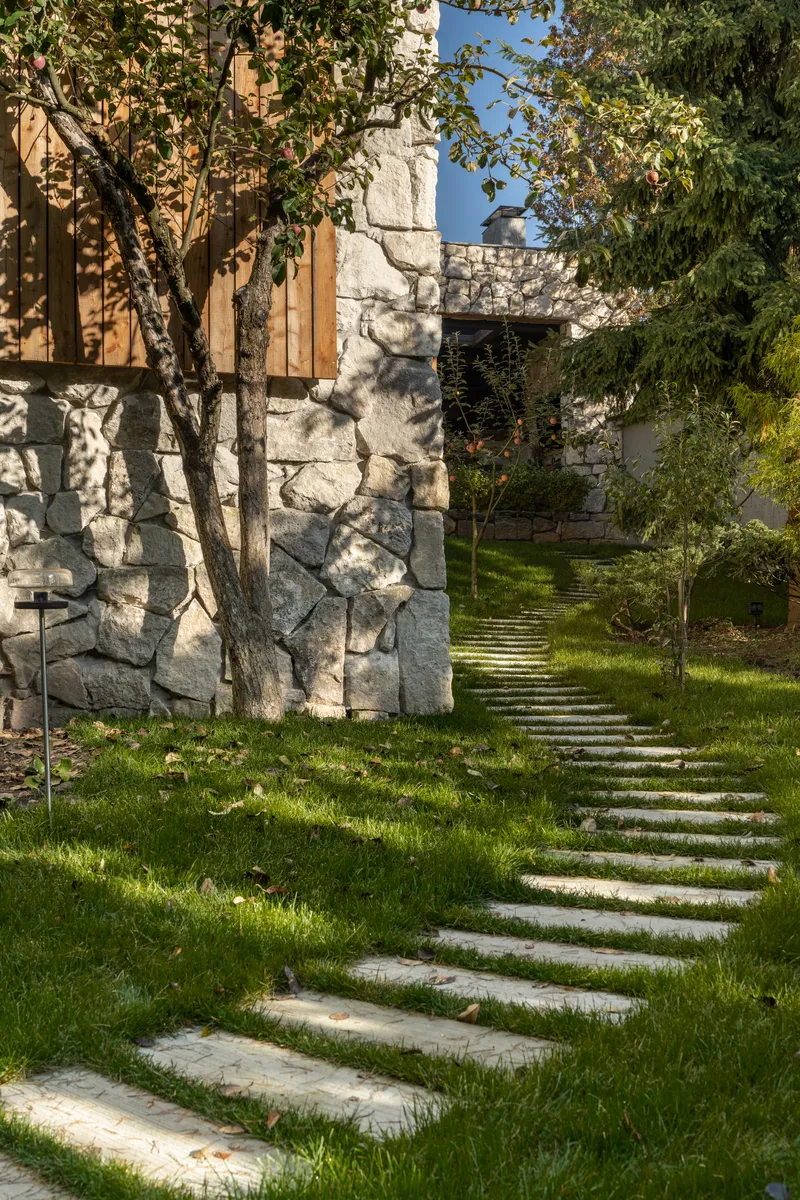 Stone paver pathway winding through sloped lawn toward rough stone wall with climbing vines