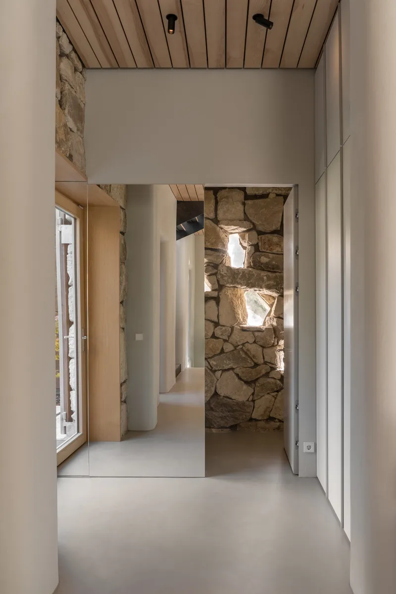 Interior hallway with slatted timber ceiling and exposed stone wall illuminated by natural light