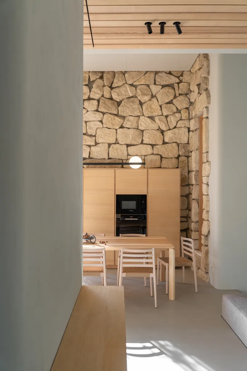 View through doorway to dining area with rough stone wall and light wood cabinetry