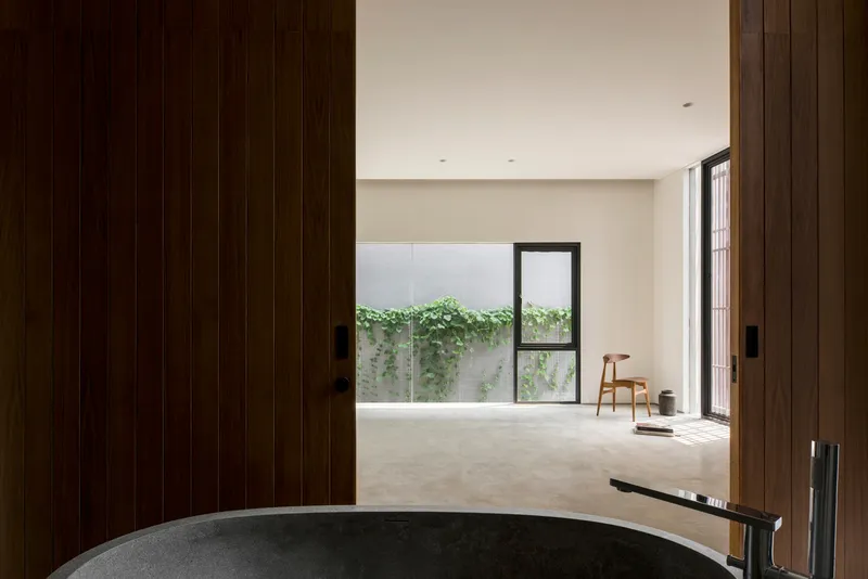 View through timber sliding doors to a polished concrete bathtub overlooking a planted courtyard