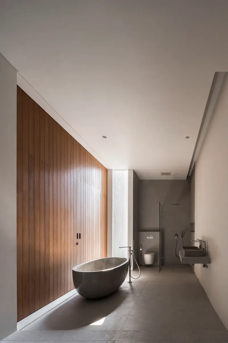 Long bathroom with freestanding stone bathtub beneath vertical timber paneling and clerestory window