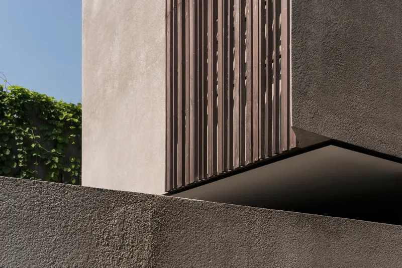 Detail of textured concrete overhang with vertical timber screen beside a planted green wall