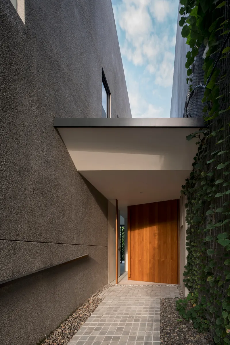 Entry path with wood door and canopy between textured concrete walls and a green wall at dusk