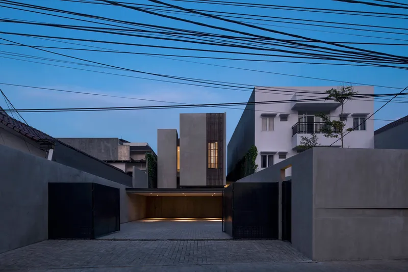 Street facade with illuminated carport and vertical window slots at twilight beneath overhead power lines