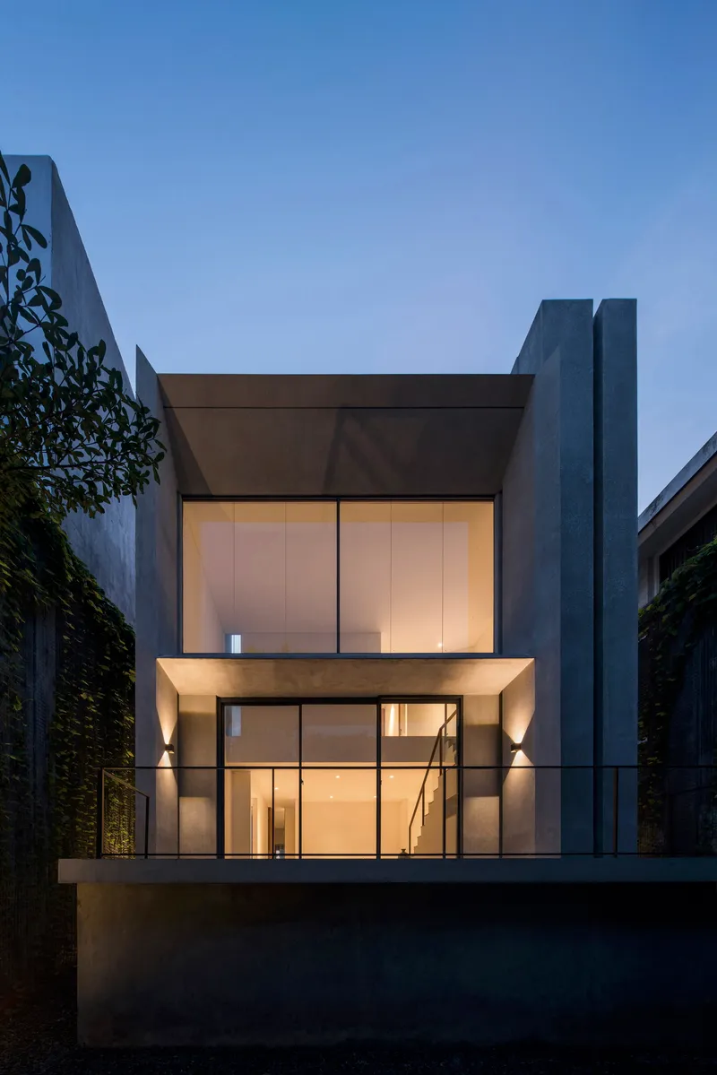 Garden elevation with two-story glass facade and cantilevered upper floor between concrete tower and green walls at twilight