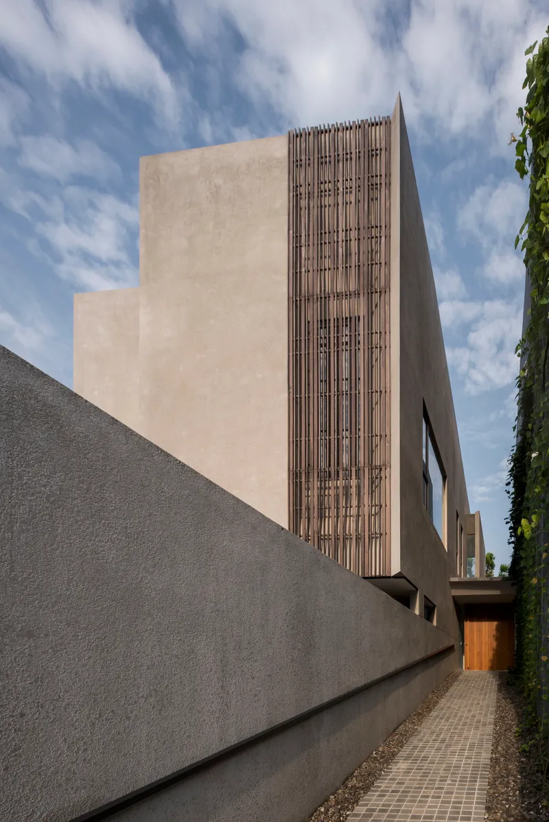 Side elevation showing the vertical timber screen panel against smooth plaster volumes under scattered clouds