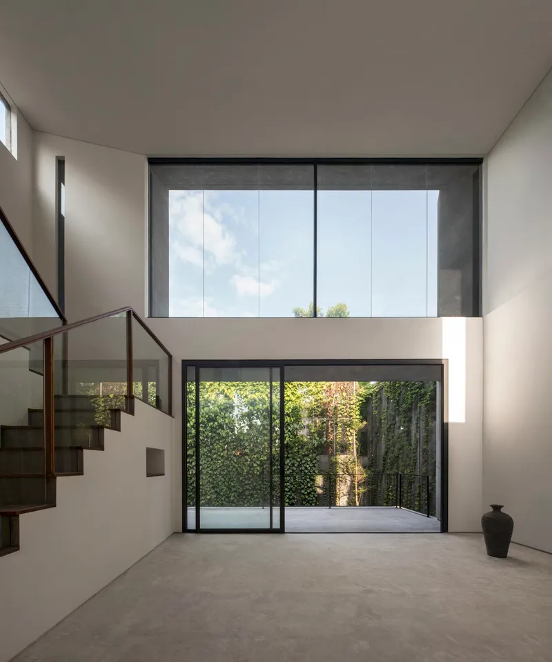 Double-height interior space with steel-framed glazing overlooking a green courtyard wall