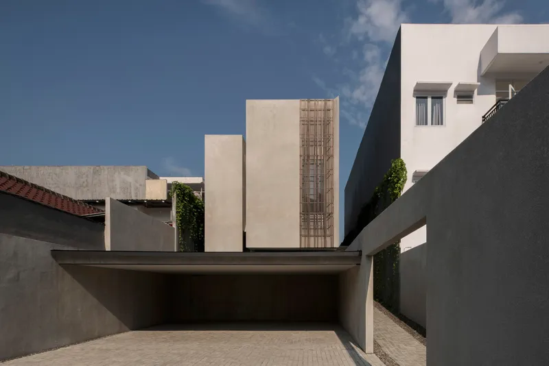 Entry courtyard framed by grey walls and the vertical timber screen under dramatic afternoon light