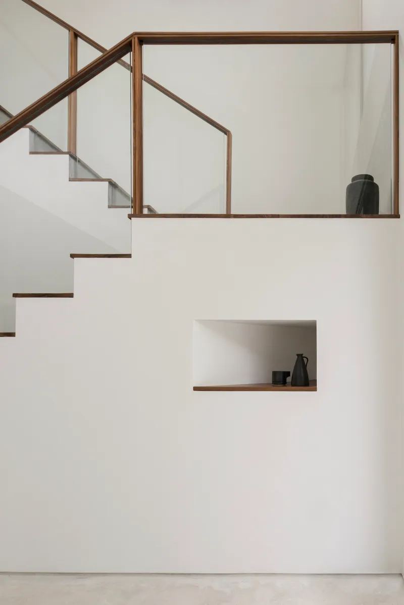 White staircase with timber-framed glass balustrade and recessed display niche holding ceramic vessels