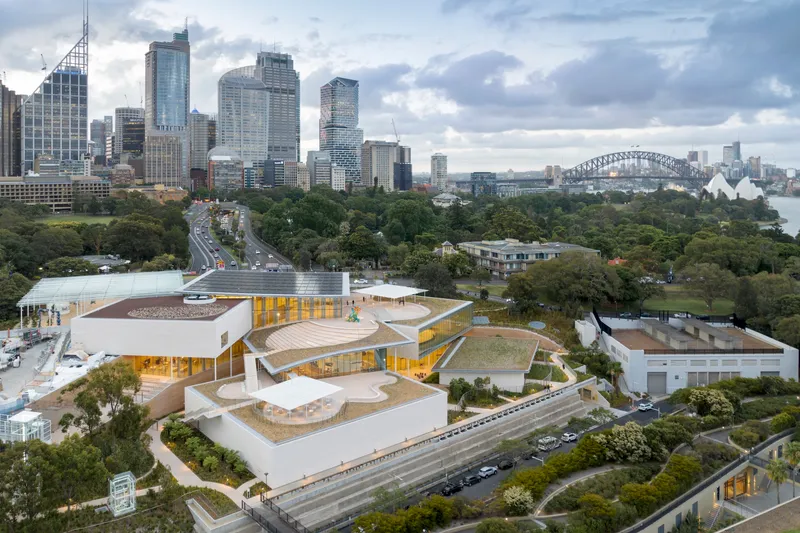 Aerial view of the terraced white volumes with golden glass walls nestled among trees and parkland